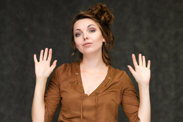 Portrait below breast over gray background of pretty young brunette woman in brown dress with beautiful hair. Standing in different poses, talking, showing with hands, demonstrating emotions.