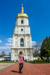 A young woman standing in front of St Sophia's Cathedral, Kiev, Ukraine. Golden rooftop of the tower. Play with the perspective, she seems as tall as the bell tower of the cathedral. Clear sky
