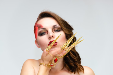 Close-up portrait on a white background of a pretty young brunette woman with beautiful makeup, with gold jewelry on her hand. Beauty, great makeup. Shows emotions.