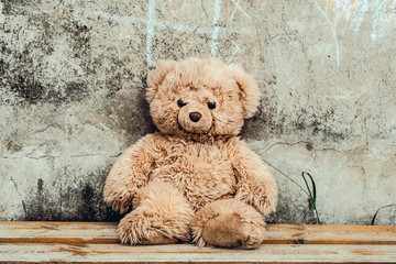 Teddy bear toy on the bench at the concrete wall with small tic tac toe game