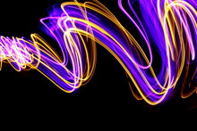 Long Exposure Photograph Of Neon Purple And Metallic Gold Colour In An Abstract Swirl Pattern Against A Black Background. Light Painting Photography.
