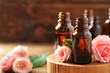 Bottles of rose essential oil and fresh flowers on table, closeup. Space for text