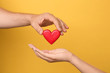 © New Africa - Man giving red heart to woman on yellow background, closeup. Donation concept
