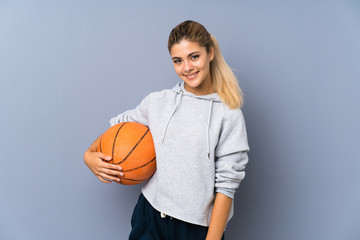 Wall Mural - Teenager girl playing basketball over grey wall smiling a lot