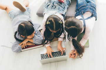 three aisan children, three sister, lay on the floor and use a laptop to do their schoolwork.childre