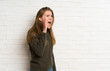 © luismolinero - Young woman over white brick wall shouting with mouth wide open