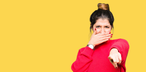 Young beautiful woman wearing red sweater and bun Laughing of you, pointing to the camera with finger hand over mouth, shame expression