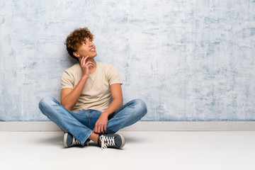 Wall Mural - Young african american man sitting on the floor thinking an idea while looking up