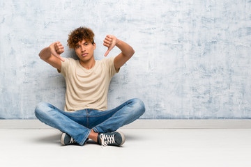 Wall Mural - Young african american man sitting on the floor showing thumb down