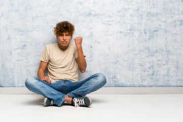 Wall Mural - Young african american man sitting on the floor with angry gesture