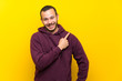 © luismolinero - Colombian man with sweatshirt over yellow wall pointing to the side to present a product