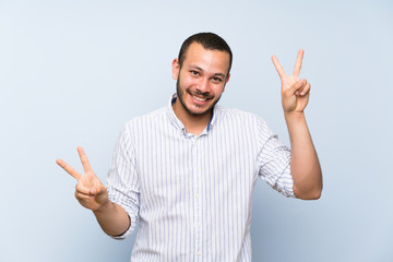 Wall Mural - Colombian man over isolated blue wall showing victory sign with both hands