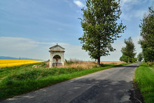 Rural Landscape With A Roadside Chapel And A Blooming Rapeseed In Poland.