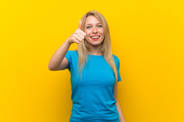 Young blonde woman over isolated yellow background with thumbs up because something good has happened