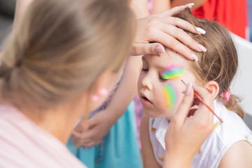 Child animator, artist's hand draws face art to little girl. Children birthday party entertainment