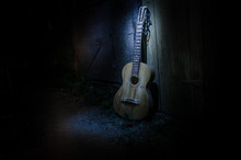 An Wooden Acoustic Guitar Is Against A Grunge Textured Wall. The Room Is Dark With A Spotlight For Your Copyspace.