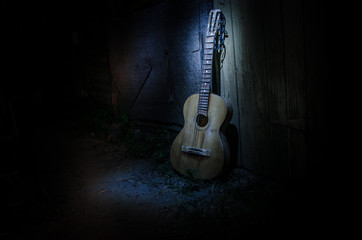 An wooden acoustic guitar is against a grunge textured wall. The room is dark with a spotlight for your copyspace.