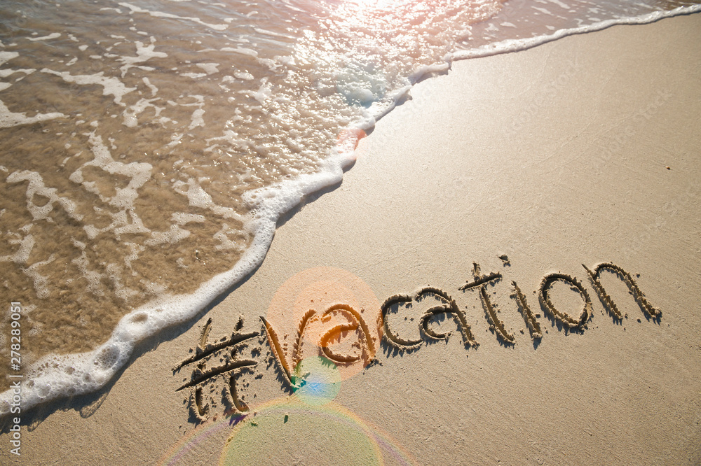 Modern travel message for the beach with a social media-friendly hashtag written with the word "vacation" in smooth sand with incoming wave - obrazy, fototapety, plakaty 