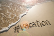 canvas print picture - Modern travel message for the beach with a social media-friendly hashtag written with the word "vacation" in smooth sand with incoming wave