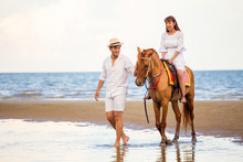 Young Couple In Love Walking With The Horse At Sea Beach On Blue Sky . Honeymoon Tropical Sea Summer Vacation. Bride Groom On The Horseback