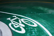 © Ivan Gener/Stocksy - Bike sign on the road in a green pavement. Curve of the entrance of parking area.