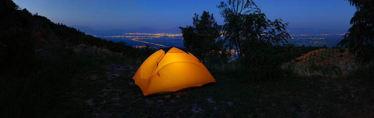 Wall Mural - orange illuminated inside tent on hill above city lights at night