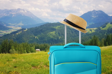 Wall Mural - recreation image of traveler luggage and fedora hat in.front of a rural landscape. holiday and vacation concept