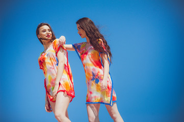 Wall Mural - Two gorgeous young women wearing swimmwear, against the blue sky