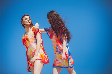 Wall Mural - Two gorgeous young women wearing swimmwear, against the blue sky