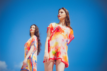 Wall Mural - Two gorgeous young women wearing swimmwear, against the blue sky