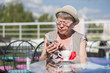 © papa - An elderly woman uses a smart phone while sitting in a summer outdoor cafe.