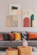 © Photographee.eu - Yellow, orange, black and brown pillows on comfortable grey scandinavian sofa in bright living room interior with abstract paintings on the wall