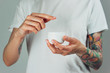 © Artem Markin - Female tattooed hands holding a jar of cream. Finger with a drop of white cream