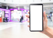 © Touchr - Woman hand holding and touching black smartphone with blank screen mockup template for your design on abstract blur department store or shopping mall.