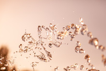 Water Droplets Frozen In The Air With Splashes And Chain Bubbles On A Golden And Bronze Isolated Background In Nature. Clear And Transparent Liquid Symbolizing Health And Nature.