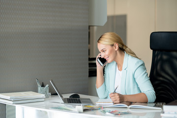 Wall Mural - Pretty blonde young designer or analyst talking on mobile phone