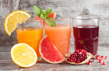 Wall Mural - Glasses of pomegranate, grapefruit, orange juice on wooden background. Refreshments and summer drinks.