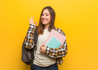 Young student woman cheerful and confident doing ok gesture