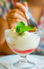 Wall Mural - young girl's hand holding a spoon and eating ice cream in glass at a table in cafe