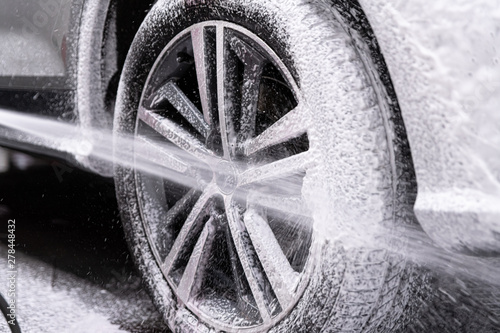 Cuadros en Lienzo Car wash worker spraying car wheel and tire with white active cleaning foam