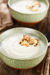 Wall Mural - Fresh homemade cream of cauliflower soup garnished with roasted cauliflower floret slices (Selective Focus, Focus on the front of the right floret on the first soup)