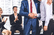 © Art_Photo - Image two business partners in elegant suit successful handshake together standing in front of group of casual business clapping hands in modern office.Partnership approval and thanks gesture concept