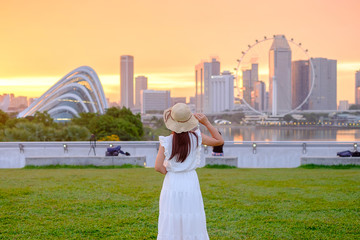 Fototapete - Young Woman traveling with hat at Sunset, happy Asian traveler visit in Singapore city downtown. landmark and popular for tourist attractions. Asia Travel concept
