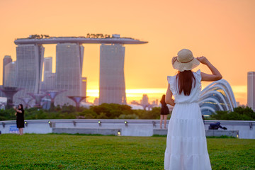 Fototapete - Young Woman traveling with hat at Sunset, happy Asian traveler visit in Singapore city downtown. landmark and popular for tourist attractions. Asia Travel concept
