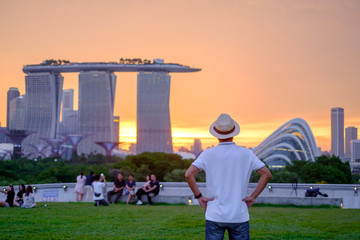 Fototapete - Young man traveling with hat at Sunset, solo Asian traveler visit in Singapore city downtown. landmark and popular for tourist attractions. Asia Travel concept