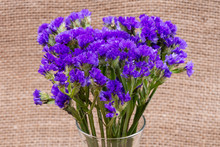 Dark Purple Statice (Limonium Sinuatum) Flowers In Clear Glass Vase On Natural Burlap Background. Mediterranean Plant In Plumbaginaceae Family.