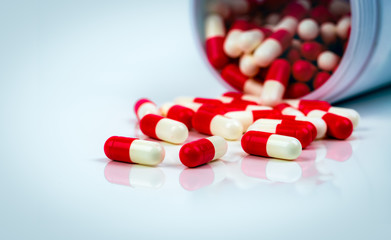 Wall Mural - Red-white capsule pills on white table on blurred background of drug bottle. Antibiotics drug resistance. Antimicrobial capsule pills. Pharmaceutical industry. Pharmacy. Global healthcare concept.