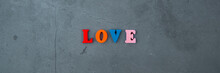 The Multicolored Love Word Is Made Of Wooden Letters On A Grey Plastered Wall Background.