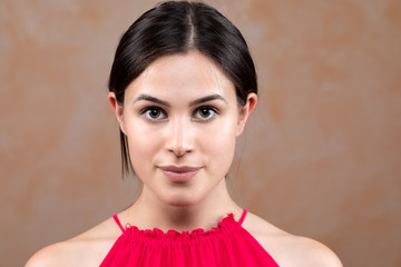 An empowered young lady stares straight into the camera. Beautiful twenty something model poses with minimal make-up and brunette hair tied back to reveal soft facial features.