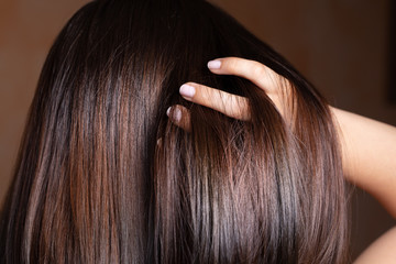 Wall Mural - A closeup view of a beautiful young Caucasian woman stroking her fingers through her long brunette straightened hair. Hairstyling before an event.